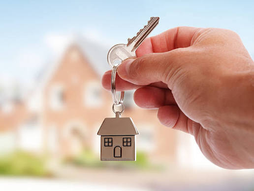 Hand holding a house key with a house in the background